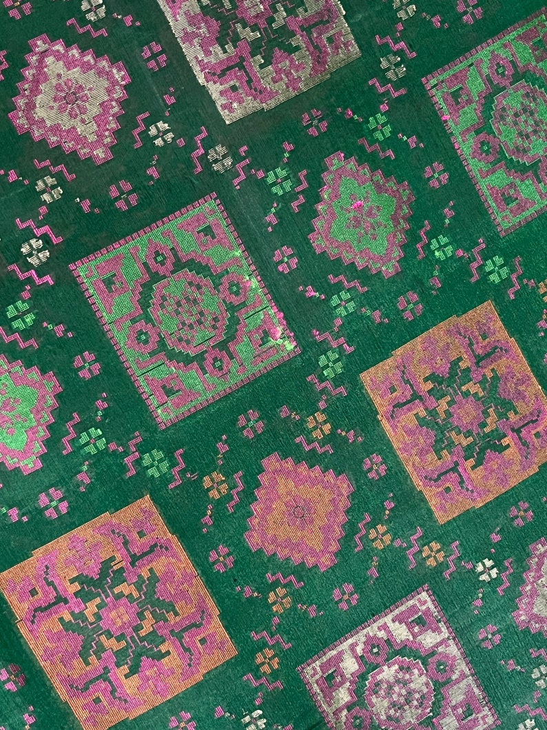 May include: Green fabric with a repeating pattern of pink, orange, and green squares. The squares have a geometric design.