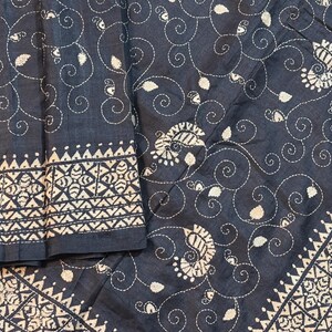 Può includere: Tessuto nero con ricamo bianco di motivi paisley e floreali. Il tessuto ha un bordo di disegni geometrici bianchi.