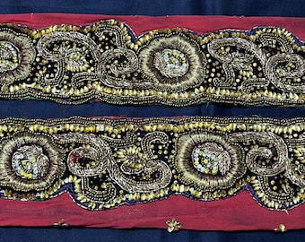 May include: Two rows of gold and black beaded trim with a paisley design. The trim is on a red fabric background.