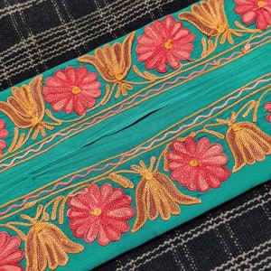 May include: Teal fabric with an embroidered floral border. The border features pink flowers with yellow and brown leaves.
