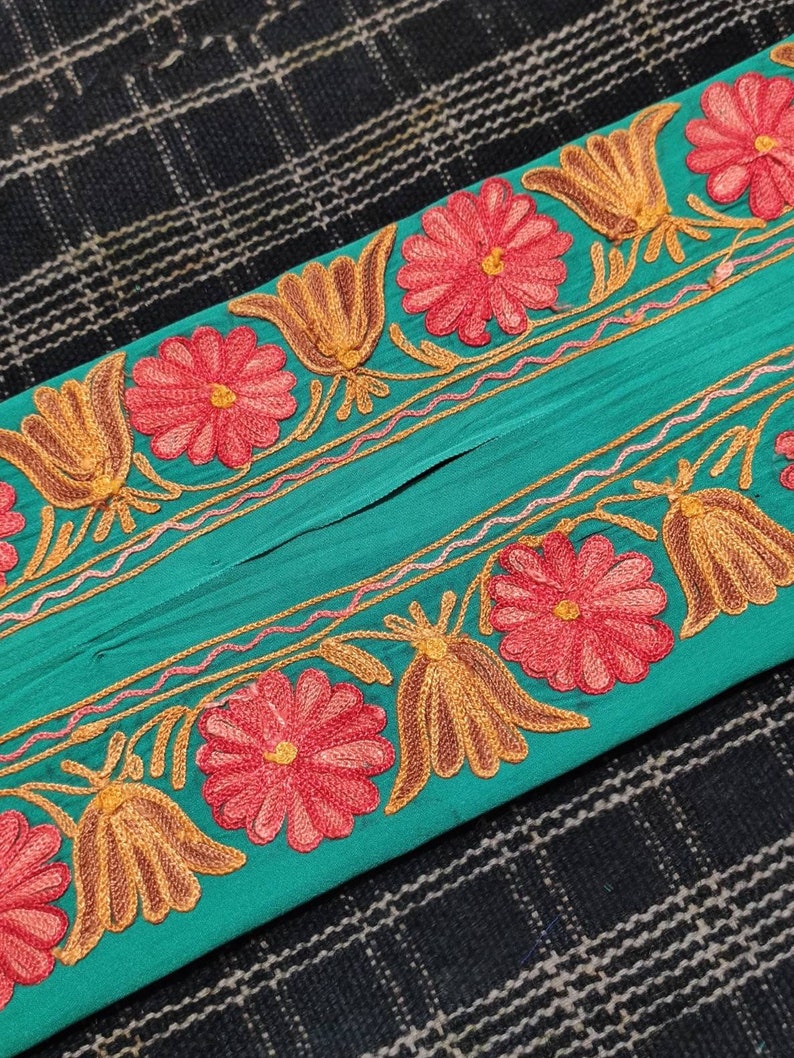May include: Teal fabric with an embroidered floral border. The border features pink flowers with yellow and brown leaves.