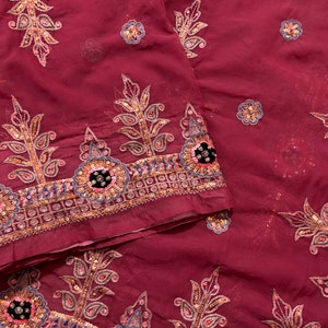 Könnte beinhalten: Ein burgunderfarbener Stoff mit aufwendiger Blumenstickerei. Der Stoff ist mit Pailletten und Perlen in Gold-, Silber- und Rosatönen verziert. Der Stoff hat eine zarte, durchscheinende Textur.