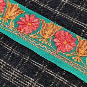 May include: Teal fabric trim with embroidered flowers and stylised tulips in shades of red, orange, and yellow.