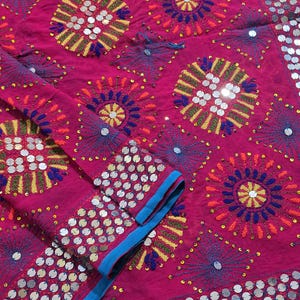 May include: A vibrant fuchsia fabric featuring intricate embroidery in yellow, orange, and blue thread. The textile is adorned with circular patterns, radiating starburst designs, and numerous small, reflective silver sequins.