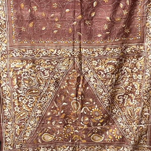 May include: A brown silk saree with intricate gold embroidery. The saree features a floral and paisley design. The border of the saree is decorated with a gold and white pattern.