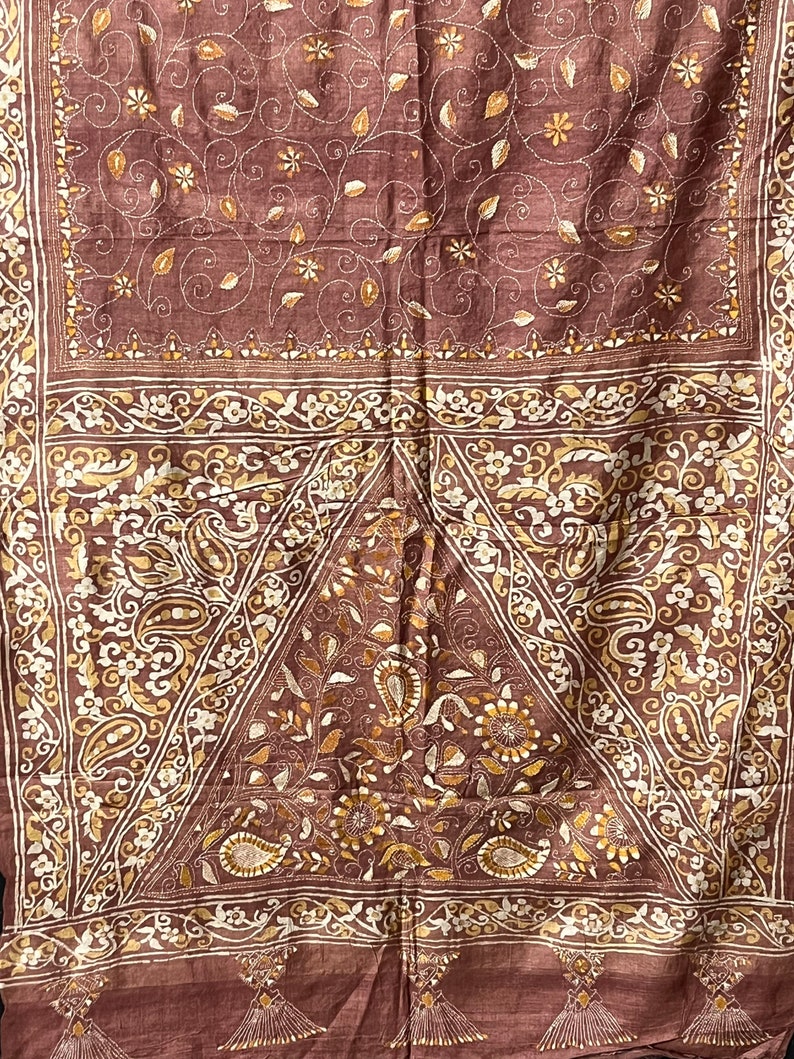 May include: A brown silk saree with intricate gold embroidery. The saree features a floral and paisley design. The border of the saree is decorated with a gold and white pattern.