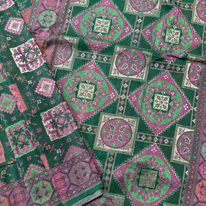 May include: Green fabric with a repeating pattern of pink and green squares and circles. The fabric has a subtle shimmer.