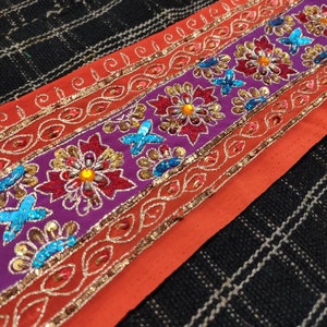 May include: Orange fabric trim with a purple band featuring embroidered flowers and sequins in shades of red, blue, gold, and silver.