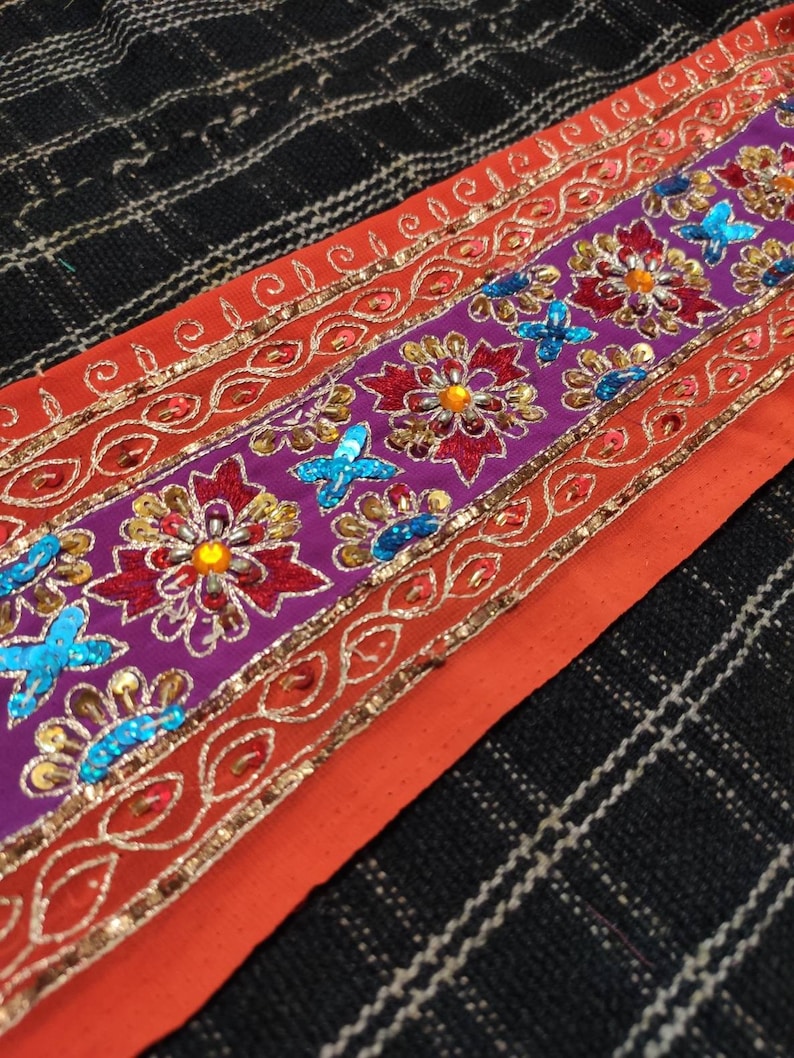 May include: Orange fabric trim with a purple band featuring embroidered flowers and sequins in shades of red, blue, gold, and silver.