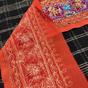 May include: Orange fabric with white and red embroidery. The fabric has a decorative border with sequins and beads.