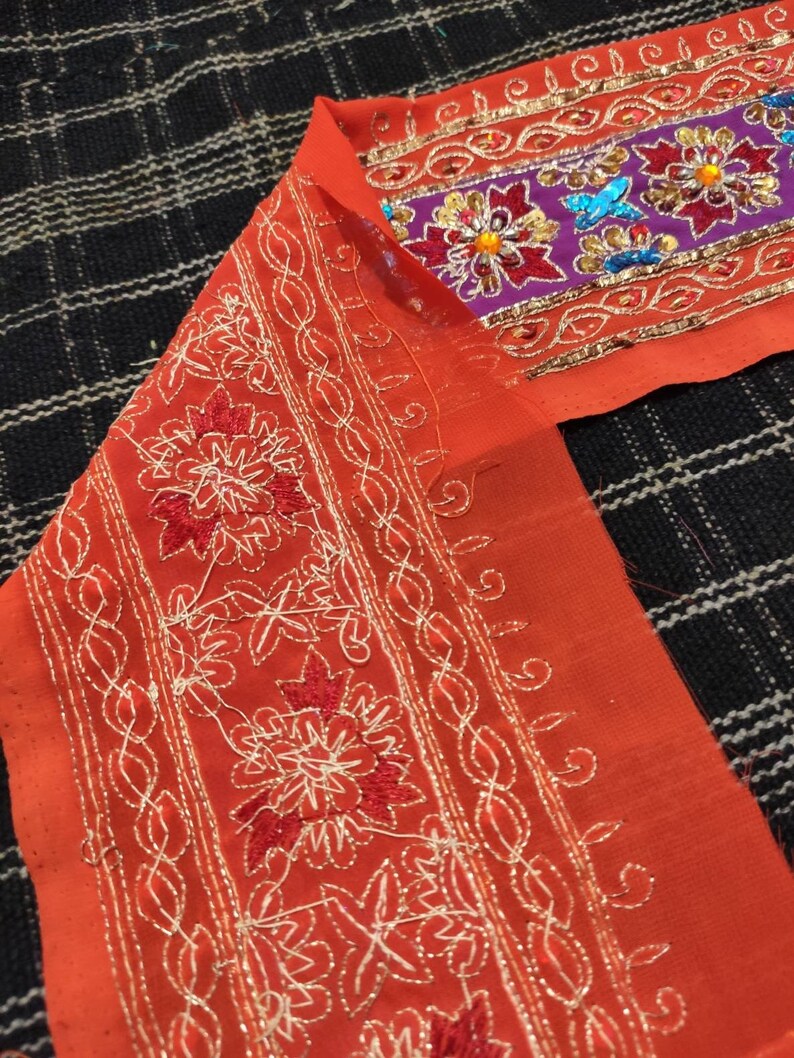 May include: Orange fabric with white and red embroidery. The fabric has a decorative border with sequins and beads.