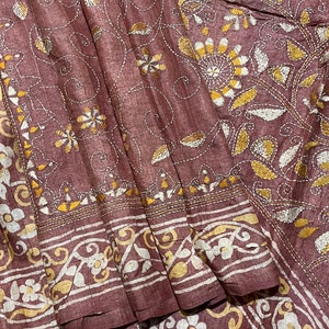 May include: A brown silk saree with intricate white and gold embroidery. The embroidery features floral and paisley designs.
