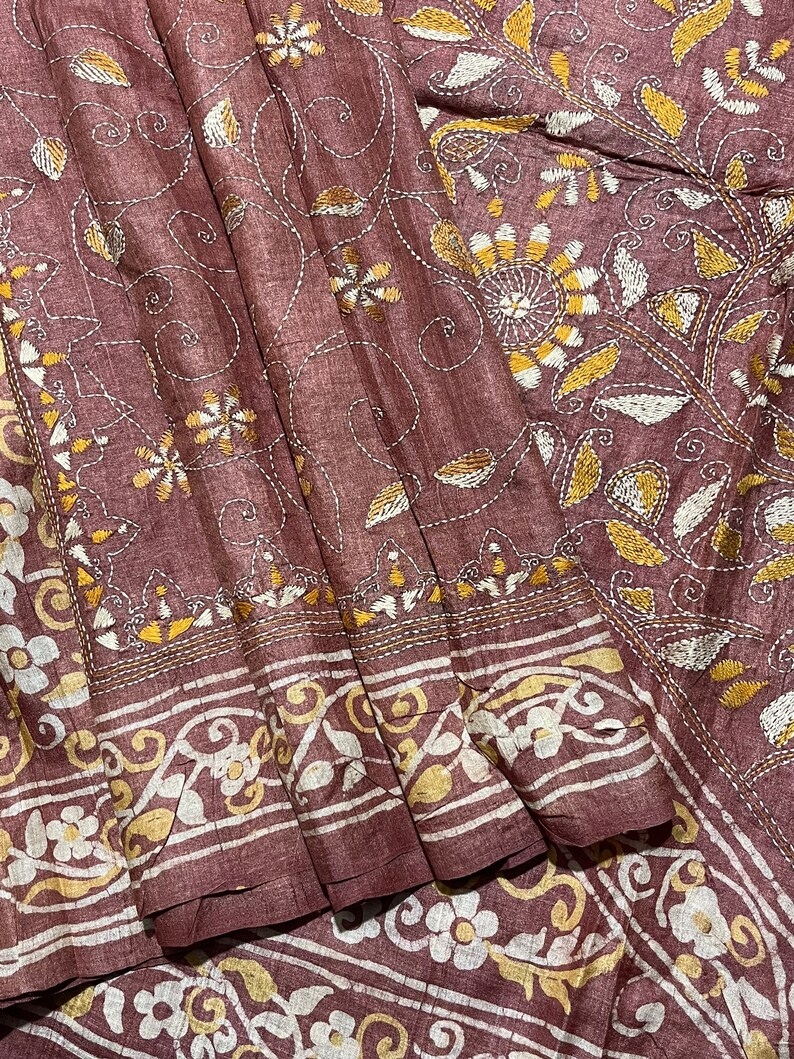 May include: A brown silk saree with intricate white and gold embroidery. The embroidery features floral and paisley designs.