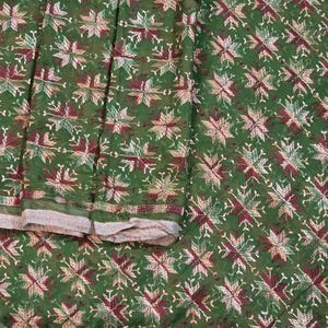 Könnte beinhalten: Ein grüner Stoff mit einem sich wiederholenden gestickten Muster aus sternartigen Formen in den Farben Kastanienbraun, Weiß und Hellgrün. Das Textil zeigt ein dichtes, symmetrisches Design mit aufwendigen Nähten auf der gesamten Oberfläche.