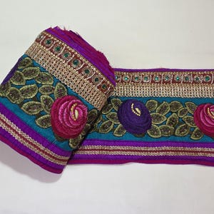 May include: A decorative trim in a rolled and flat section. The trim features teal, purple, and gold colours, with embroidered leaves and flowers. Small green and gold accents embellish the trim.