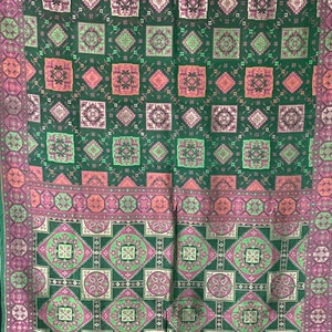 May include: Green fabric with a repeating pattern of pink, white, and green squares. The fabric has a border of pink, white, and green geometric shapes.