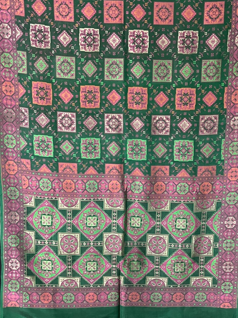 May include: Green fabric with a repeating pattern of pink, white, and green squares. The fabric has a border of pink, white, and green geometric shapes.
