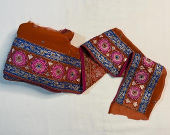 May include: A brown fabric trim with blue, silver, and pink embroidery. The trim features a repeating pattern of floral designs.