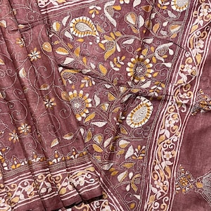 May include: A brown silk saree with intricate white and gold embroidery. The embroidery features floral patterns and paisley designs.