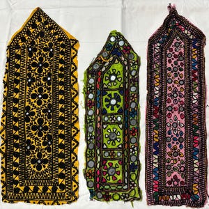 Puede incluir: Tres paneles de tela bordada con patrones geométricos y adornos de espejo. Los paneles son amarillos, verdes y rosas con bordados negros.