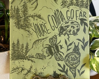 May include: A rectangular canvas painting with a light green background featuring dark green line art of mountains, pine trees, a small cabin, a ladybug, a bee, and a snail. The text "YOU'RE GONNA GO FAR" is printed in the centre.