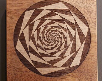 May include: Square wooden coaster with a geometric spiral design. The coaster features a dark brown circular border and a light brown spiral pattern in the center. The wood has a natural grain.