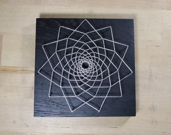 May include: A geometric design created with string wrapped around nails hammered into a black wooden board.