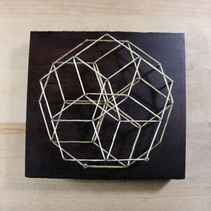 May include: A geometric string art piece with white and yellow string stretched between nails on a dark wood background.