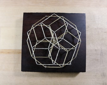 May include: A geometric string art piece with white and yellow string stretched between nails on a dark wood background.