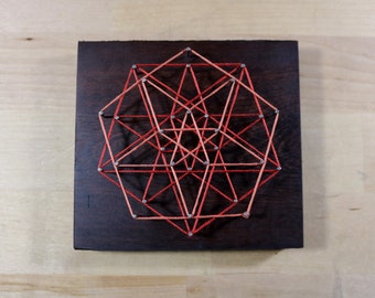 May include: A geometric design created with string art on a dark wood background. The design features a series of triangles and squares connected by red and orange string.