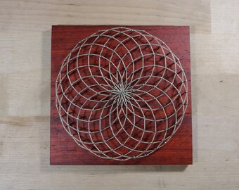 May include: A circular string art design with a geometric pattern on a dark red wooden background.