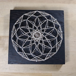 May include: A geometric string art design with a white string wrapped around silver nails on a black wooden background.