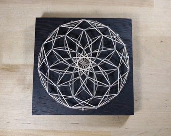 May include: A geometric string art design with a white string wrapped around silver nails on a black wooden background.