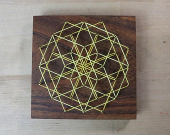 May include: A geometric design created with yellow string stretched between gold tacks on a dark wood background.
