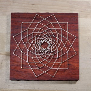 May include: A geometric design created with string art on a dark red wooden board. The design is a series of concentric squares with lines connecting the corners.