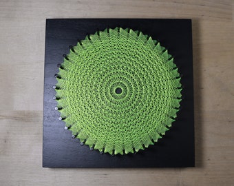 May include: A green string art design in the shape of a circle on a black background.