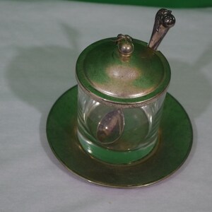 Könnte beinhalten: Ein versilberter Glas-Zuckerstreuer mit Deckel und einem kleinen Löffel. Der Streuer steht auf einer versilberten Untertasse.