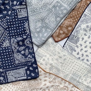 Puede incluir: Una colecci&oacute;n de telas superpuestas con varios patrones de cachemira en azul marino, gris claro, marr&oacute;n y crema. Cada tela cuadrada muestra intrincados dise&ntilde;os impresos en blanco o oscuro con una textura acolchada visible y bordes acabados.