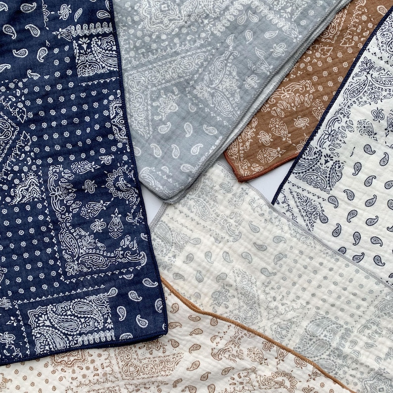 Puede incluir: Una colecci&oacute;n de telas superpuestas con varios patrones de cachemira en azul marino, gris claro, marr&oacute;n y crema. Cada tela cuadrada muestra intrincados dise&ntilde;os impresos en blanco o oscuro con una textura acolchada visible y bordes acabados.