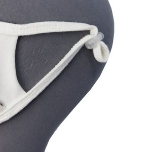 May include: Close-up of a white face mask with adjustable ear loops. The ear loops are attached to the mask with small, clear plastic adjusters. The mask is made of a soft, white fabric.