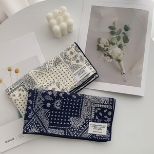 May include: Two rectangular fabric cloths featuring a dark blue and white paisley bandana pattern. Each cloth has a white fabric label sewn on the corner that reads HANDMADE BY AVO, SIMPLY MADE, WORTH KEEPING, MADE WITH CARE in black text.
