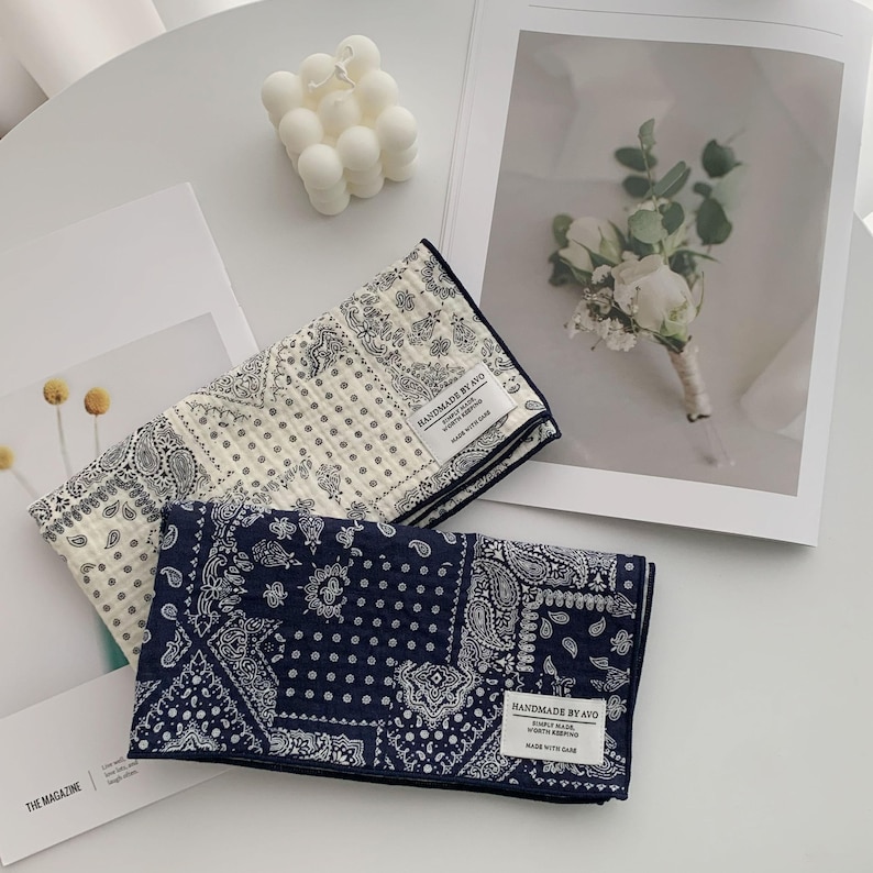 May include: Two rectangular fabric cloths featuring a dark blue and white paisley bandana pattern. Each cloth has a white fabric label sewn on the corner that reads HANDMADE BY AVO, SIMPLY MADE, WORTH KEEPING, MADE WITH CARE in black text.