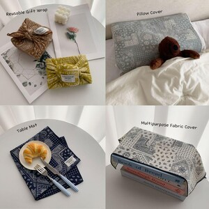 May include: A collection of fabric items featuring paisley patterns: two reusable gift wraps in brown and yellow, a gray pillow cover with a brown teddy bear, a navy blue table mat with a croissant and cutlery, and a gray multipurpose fabric cover.