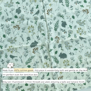 May include: A white cotton gauze fabric featuring a repeating pattern of green and brown botanical illustrations, including various leaves, flowers, birds, squirrels, and rabbits. The fabric has a textured, crinkled appearance throughout the surface.