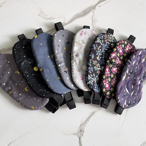 Op de afbeelding: Een set van tien slaapmaskers met verschillende patronen, waaronder sterren, manen, bloemenpatronen en geometrische vormen. De maskers zijn gemaakt van zacht materiaal en hebben verstelbare bandjes.