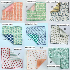 May include: A collection of nine square fabric cloths featuring various patterns including orange slices, limes, hydrangea blooms, lemons, eggplants, avocados, camellias, carrots, and sunflowers, each with a contrasting patterned reverse side.
