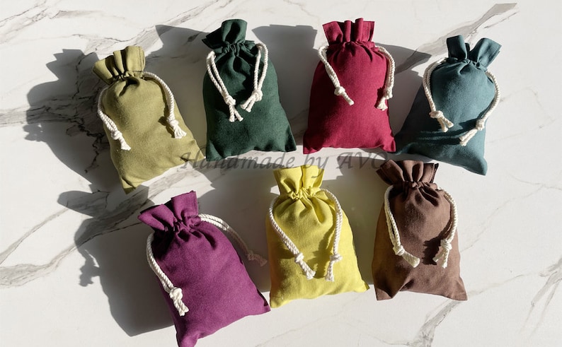 K&ouml;nnte beinhalten: Acht kleine Beutel mit Kordelzug in verschiedenen Farben, darunter Gr&uuml;n, Rot, Braun, Gelb und Lila. Die Beutel sind aus weichem Stoff gefertigt und haben wei&szlig;e Kordelz&uuml;ge.
