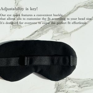 Op de afbeelding: Zwarte oogmasker met een verstelbare band en gesp. De band is gemaakt van zwart elastiek en heeft een gespsluiting. Het masker is ontworpen om licht te blokkeren en een comfortabele pasvorm te bieden.