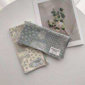 May include: Two rectangular cotton cloths featuring a grey and white paisley pattern. Each cloth has a quilted texture and a white fabric label stitched to the corner that reads HANDMADE BY AVO, SIMPLY MADE, WORTH KEEPING, MADE WITH CARE.