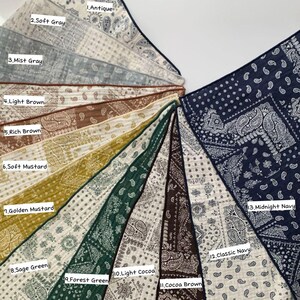 May include: A collection of thirteen square fabric bandanas arranged in a fan shape, each featuring a white paisley pattern. Colors include Antique, Soft Gray, Mist Gray, Light Brown, Rich Brown, Soft Mustard, Golden Mustard, Sage Green, Forest Green, Light Cocoa, Cocoa Brown, Classic Navy, and Midnight Navy.